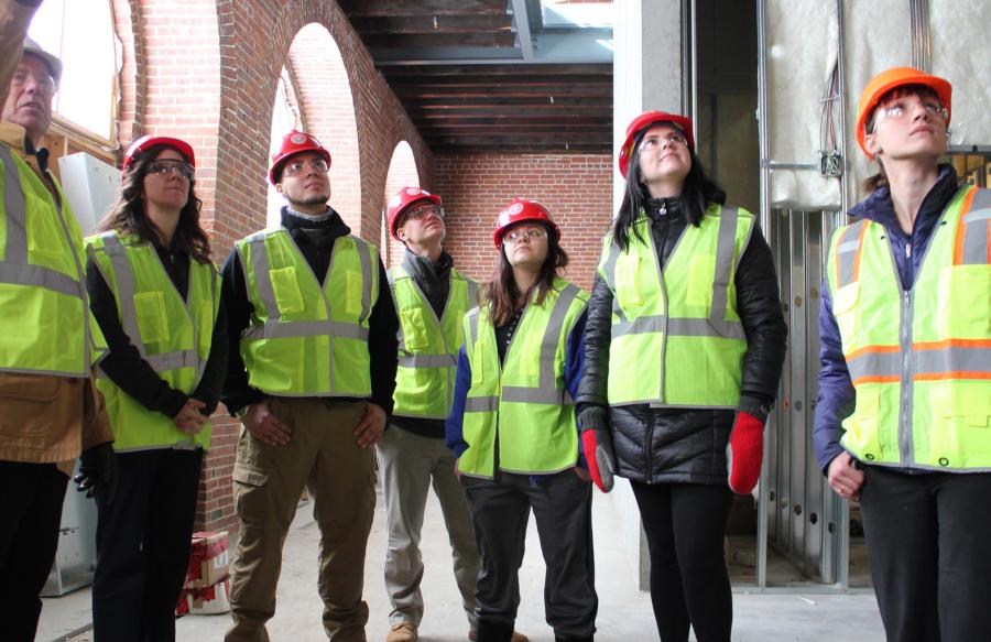 学生们戴着安全帽，穿着反光背心观察建筑